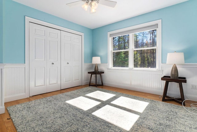 bedroom with ceiling fan, a closet, wood finished floors, and wainscoting