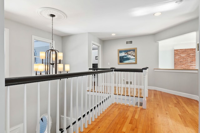 hallway with visible vents, an upstairs landing, wood finished floors, baseboards, and a chandelier