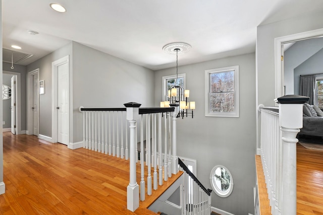 hall with baseboards, attic access, an upstairs landing, wood finished floors, and a notable chandelier