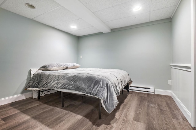 bedroom featuring baseboard heating, a paneled ceiling, baseboards, and wood finished floors