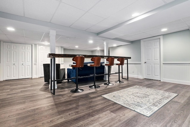 bar with a paneled ceiling, wood finished floors, a dry bar, and wainscoting