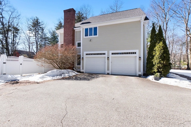 snow covered property with fence, a garage, driveway, and a chimney