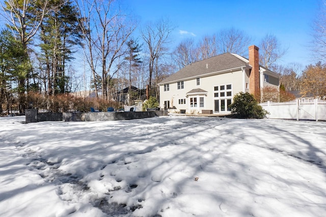 snow covered rear of property featuring a chimney and fence