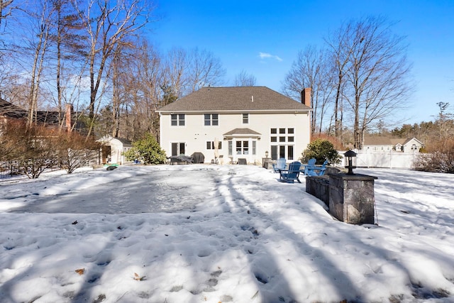 snow covered rear of property featuring a chimney and fence