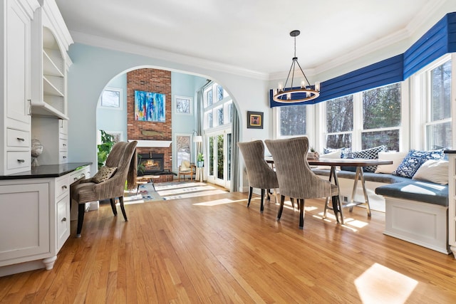 dining area featuring breakfast area, light wood-type flooring, a brick fireplace, and ornamental molding