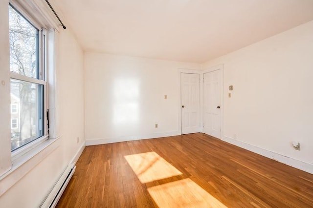 unfurnished room with baseboard heating, baseboards, and wood finished floors