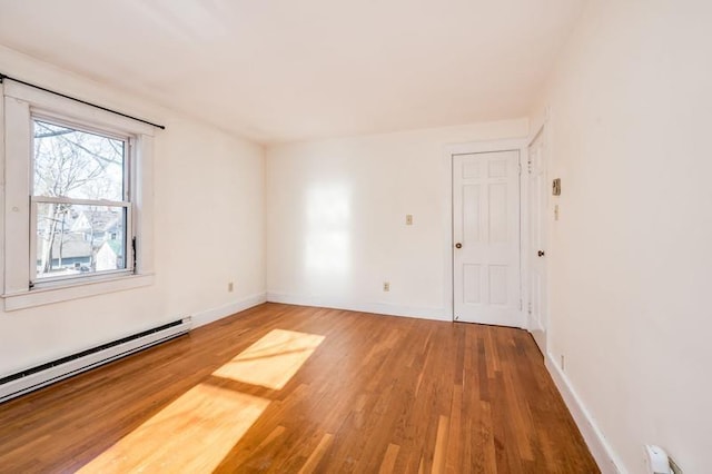 empty room with baseboard heating, baseboards, and wood finished floors