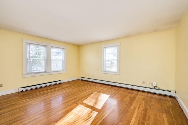 empty room with a baseboard heating unit, baseboards, and wood finished floors