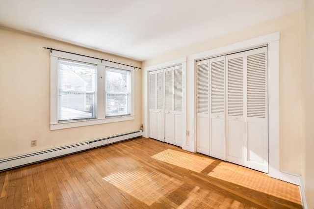 unfurnished bedroom featuring a baseboard heating unit, two closets, and hardwood / wood-style floors