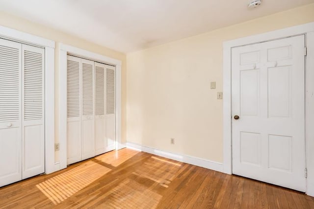 unfurnished bedroom featuring light wood-style floors, baseboards, and two closets