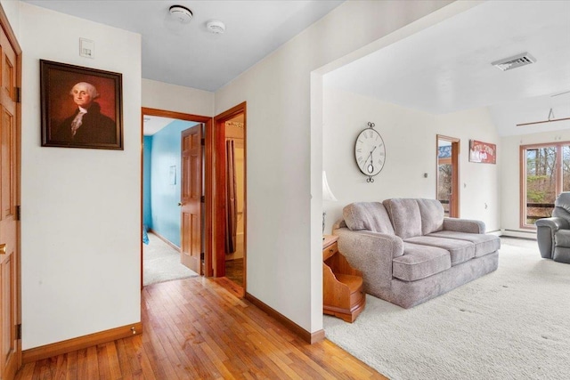 hall featuring visible vents, baseboards, light wood-style floors, and a baseboard radiator