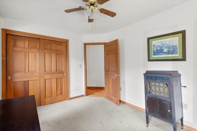 unfurnished bedroom featuring a closet, light colored carpet, a ceiling fan, and baseboards