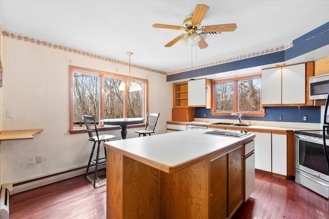 kitchen featuring wallpapered walls, a baseboard heating unit, white cabinets, stainless steel appliances, and a sink