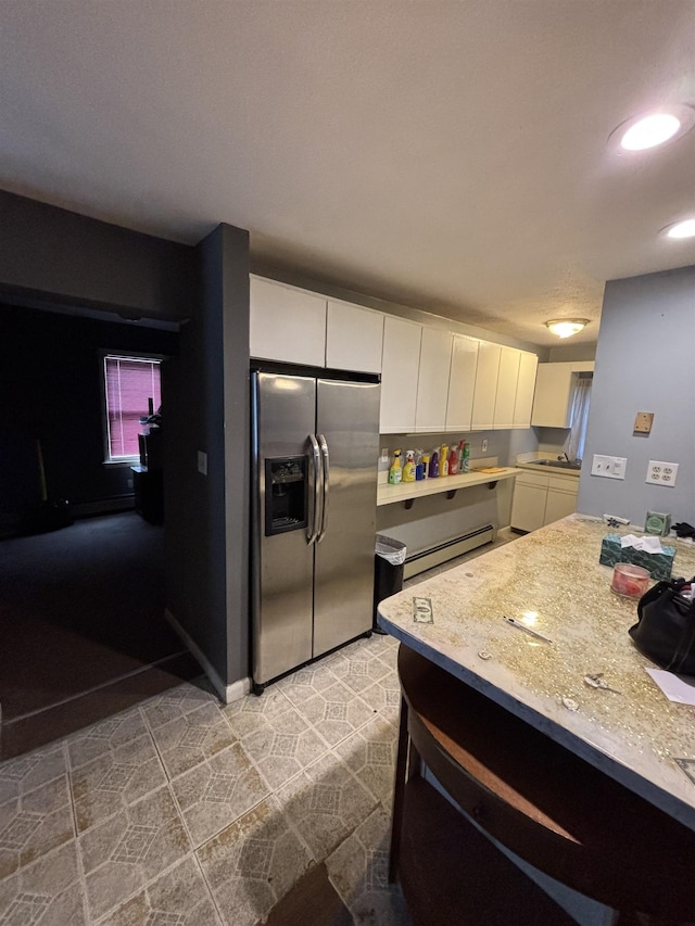 kitchen featuring a baseboard radiator, light tile patterned flooring, stainless steel fridge, white cabinetry, and a sink