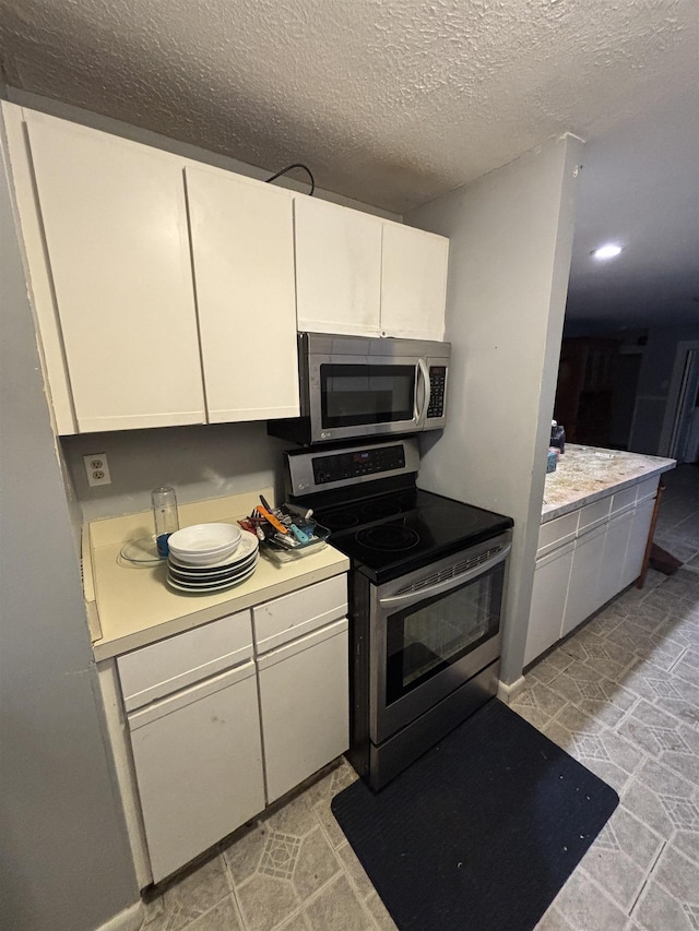 kitchen with baseboards, stainless steel appliances, light countertops, a textured ceiling, and white cabinetry