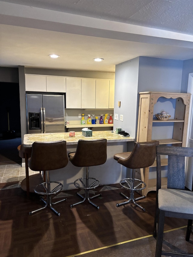 kitchen featuring a kitchen breakfast bar, recessed lighting, a peninsula, white cabinets, and stainless steel fridge with ice dispenser