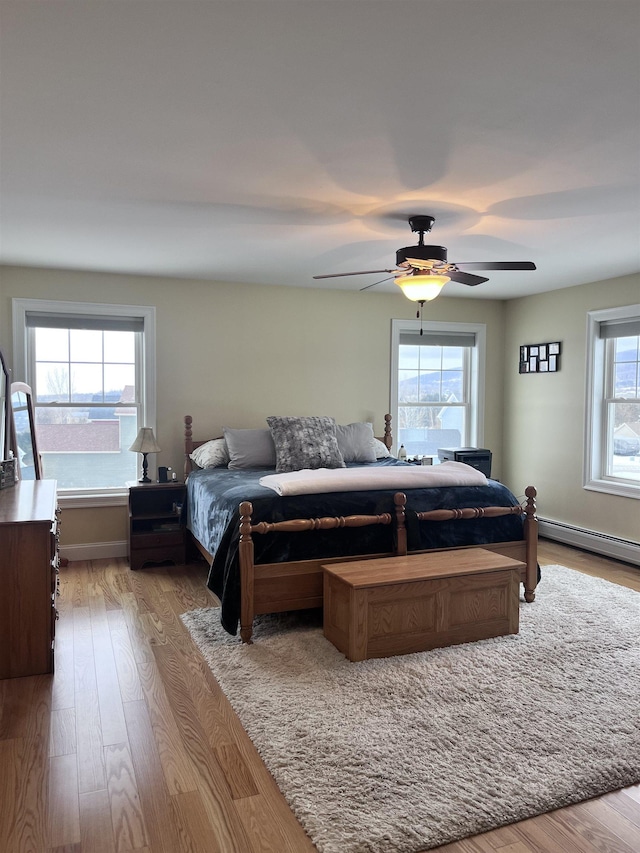 bedroom with a ceiling fan, wood finished floors, baseboards, and a baseboard radiator