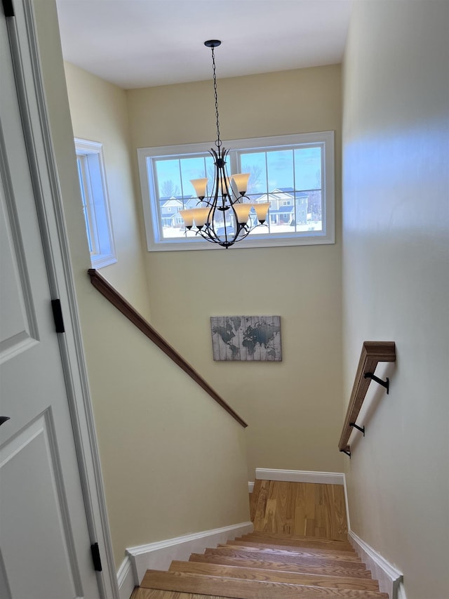 staircase with a chandelier, baseboards, and wood finished floors