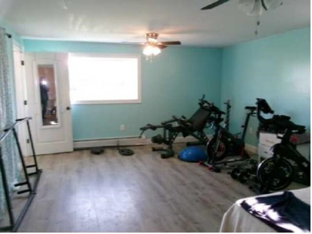 exercise area with a baseboard radiator, wood finished floors, and ceiling fan