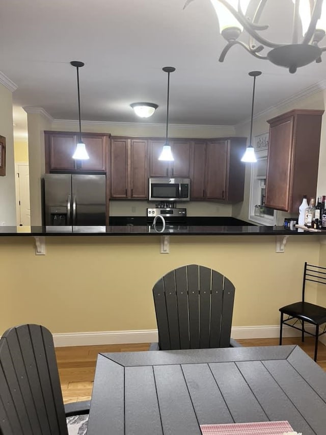 kitchen with dark countertops, wood finished floors, stainless steel appliances, crown molding, and hanging light fixtures