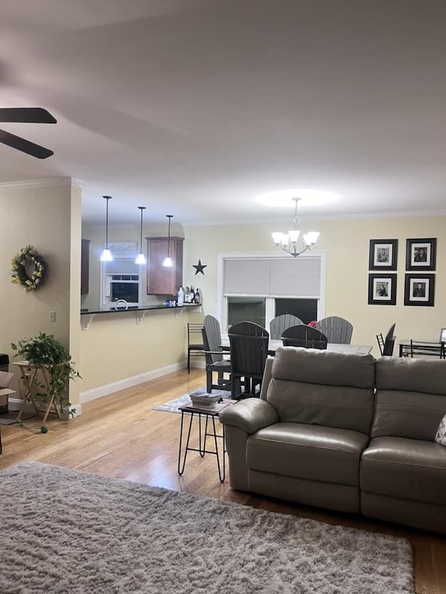 living area with light wood-style flooring, ceiling fan with notable chandelier, crown molding, and baseboards