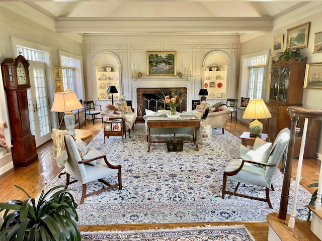 living area featuring beam ceiling, a brick fireplace, crown molding, and wood finished floors