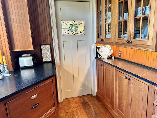 kitchen featuring dark countertops, brown cabinetry, glass insert cabinets, and light wood-style floors