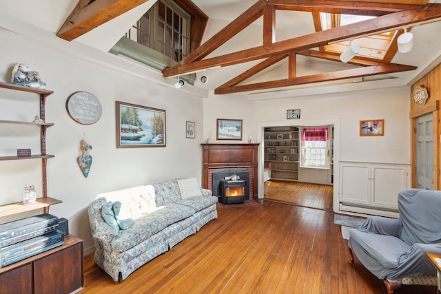 living area with wood-type flooring, vaulted ceiling with beams, and a wood stove