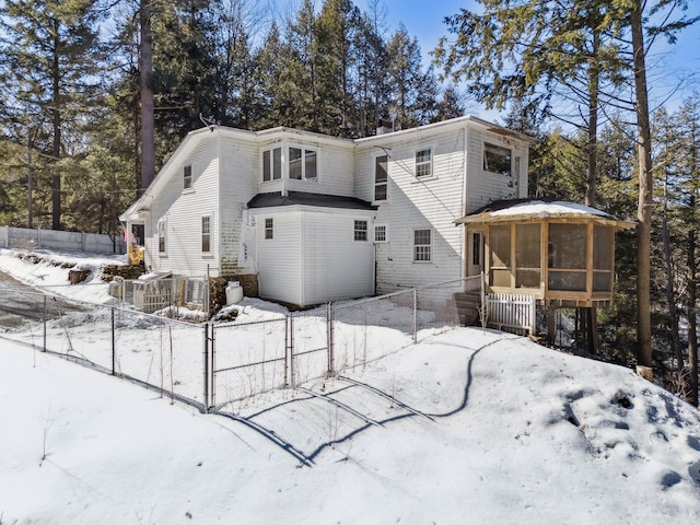 snow covered back of property with a gate, fence, and a sunroom