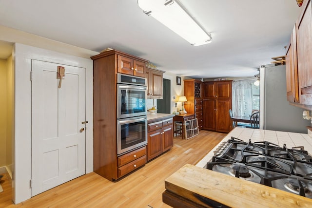 kitchen with tile counters, brown cabinetry, light wood-style floors, and appliances with stainless steel finishes