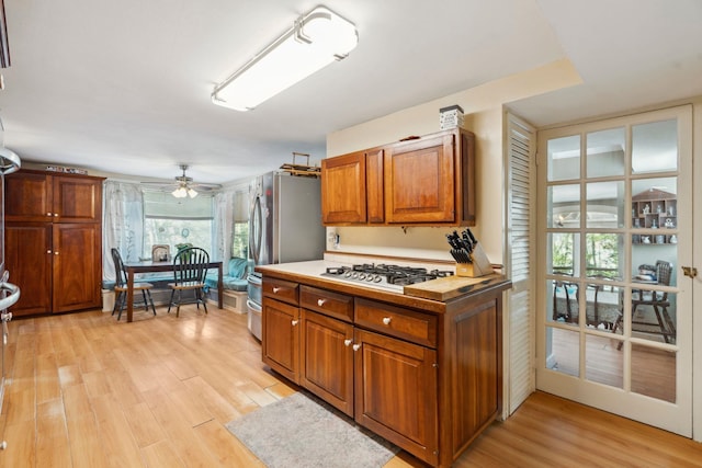 kitchen featuring stainless steel appliances, a ceiling fan, brown cabinetry, and light wood finished floors