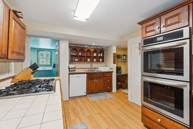 kitchen with light wood-style flooring, a sink, gas stovetop, stainless steel double oven, and dishwasher