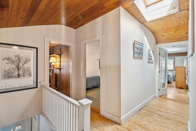 hall with lofted ceiling with skylight, light wood-style floors, baseboards, and wooden ceiling