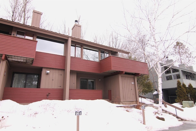 view of front facade with a balcony, board and batten siding, and a chimney