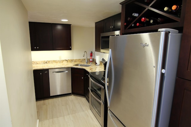 kitchen with light stone counters, dark brown cabinets, appliances with stainless steel finishes, and a sink