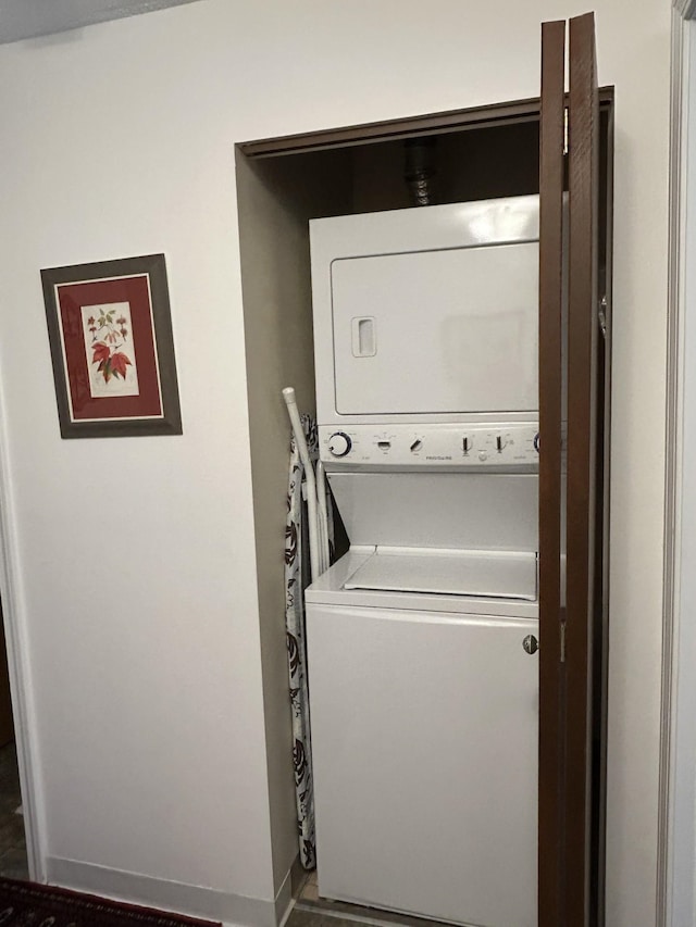 clothes washing area with baseboards, laundry area, and stacked washer / dryer