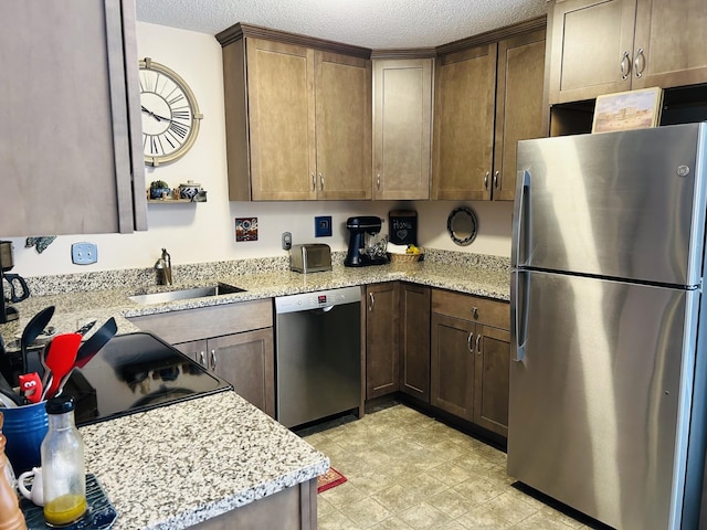 kitchen featuring a sink, stainless steel appliances, light stone countertops, and a textured ceiling