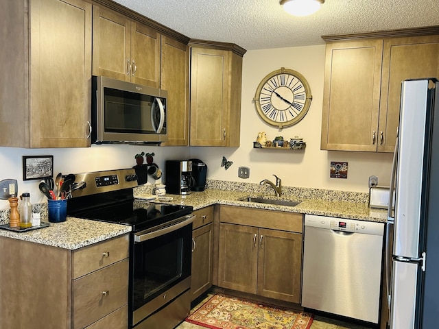 kitchen with light stone counters, a textured ceiling, stainless steel appliances, and a sink