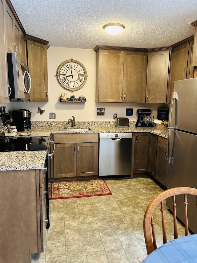 kitchen featuring a textured ceiling, light stone countertops, appliances with stainless steel finishes, and a sink