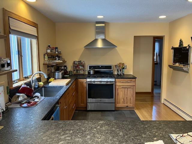 kitchen with a sink, stainless steel appliances, wall chimney exhaust hood, brown cabinets, and baseboard heating