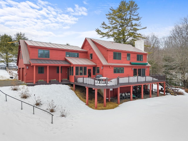 snow covered back of property with stairs, a chimney, metal roof, a deck, and a standing seam roof