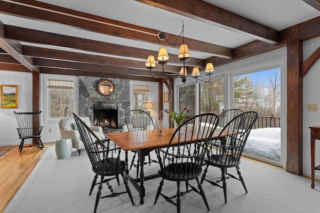 dining area featuring beam ceiling, a notable chandelier, wood finished floors, a stone fireplace, and baseboards