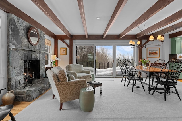 living area featuring beamed ceiling, a notable chandelier, and a stone fireplace