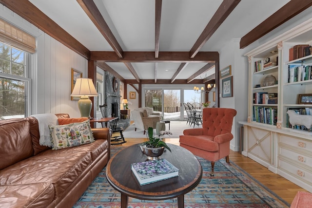 living room with beam ceiling, a notable chandelier, wood finished floors, and a large fireplace