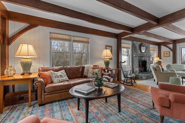 living area with beam ceiling, a stone fireplace, and wood finished floors