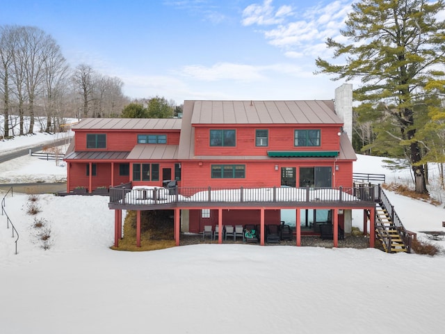 snow covered back of property with stairway, metal roof, a deck, and a standing seam roof