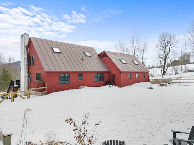 snow covered property featuring metal roof, a chimney, and a standing seam roof