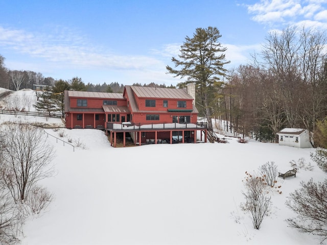 snow covered property with an outbuilding, a standing seam roof, a chimney, a deck, and metal roof