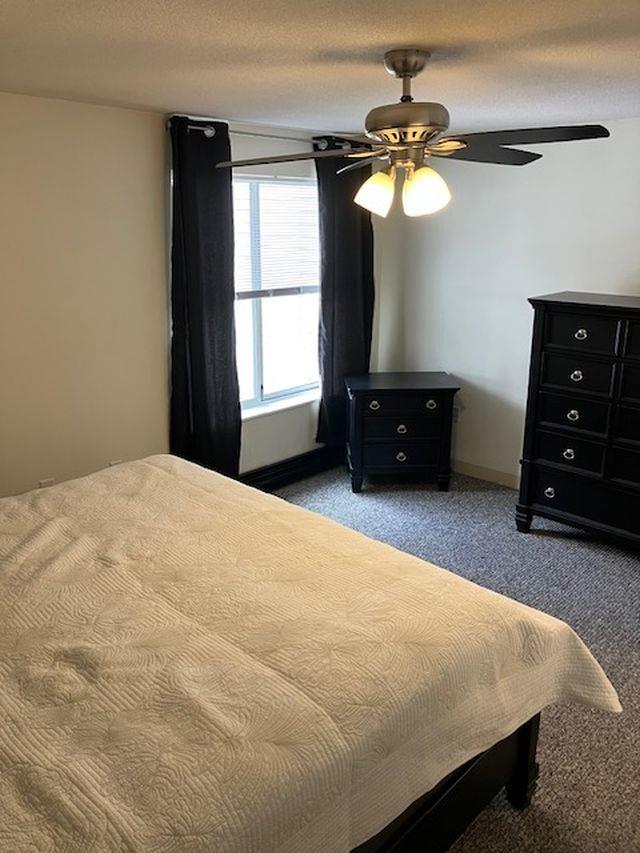 carpeted bedroom with ceiling fan and a textured ceiling