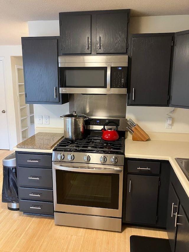 kitchen with light wood finished floors, appliances with stainless steel finishes, a textured ceiling, and light countertops